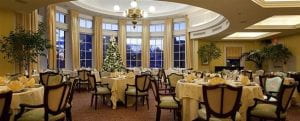 Ballroom of the Hope Club with a large wall of windows in a circular rotunda, a Christmas tree against the far wall of windows, and circular dinner tables with white linens.