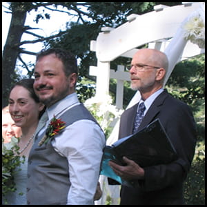 John Urban and Jen Johnson stands at a wedding alter with an officiant behind them