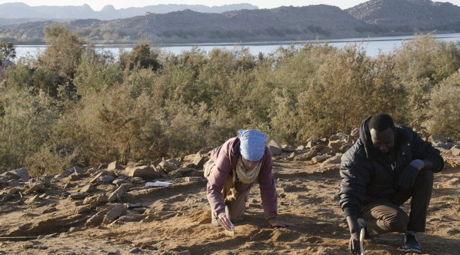 two archaeologists on knees brushing rocks on the ground