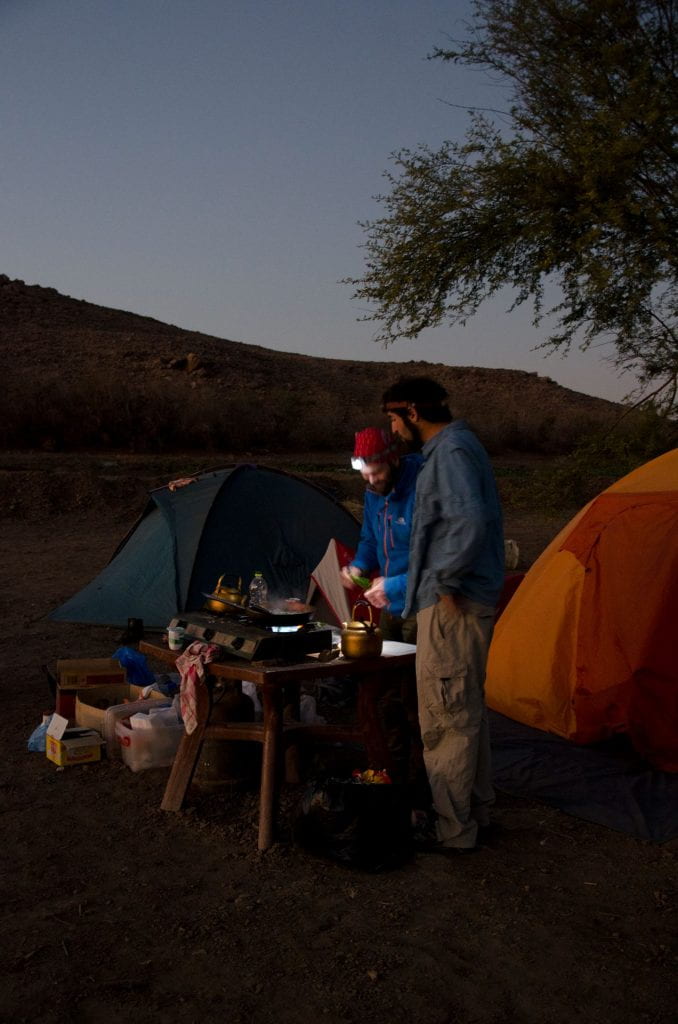 camping tents and two men with headlamps bending over a stove