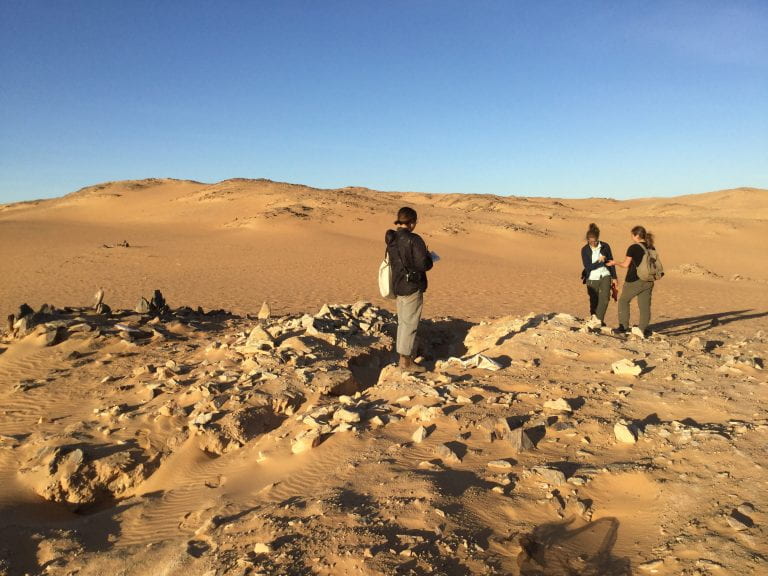 women standing in rocky desert looking at ground
