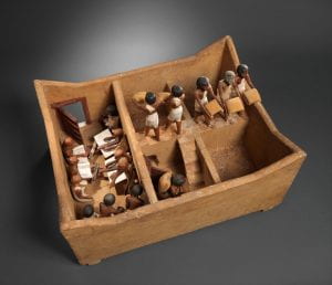 ancient wooden model like a doll's house with people emptying bags of grain into square rooms with no roof
