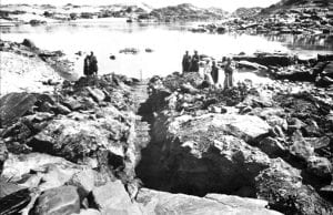 black and white archival photo showing stairs carved into bedrock with Egyptian workmen standing near the river
